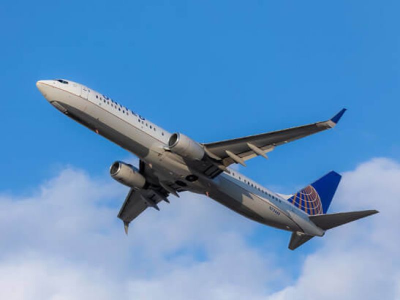 Imagem de um avião voando no céu azul e com nuvens brancas
