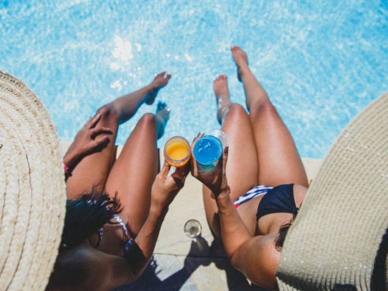 Imagem de duas mulheres brindando na beira de uma piscina