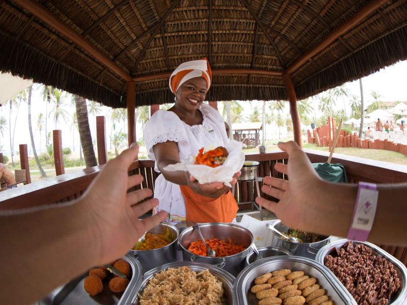Imagem de uma pessoa oferecendo comidas da Bahia para outra