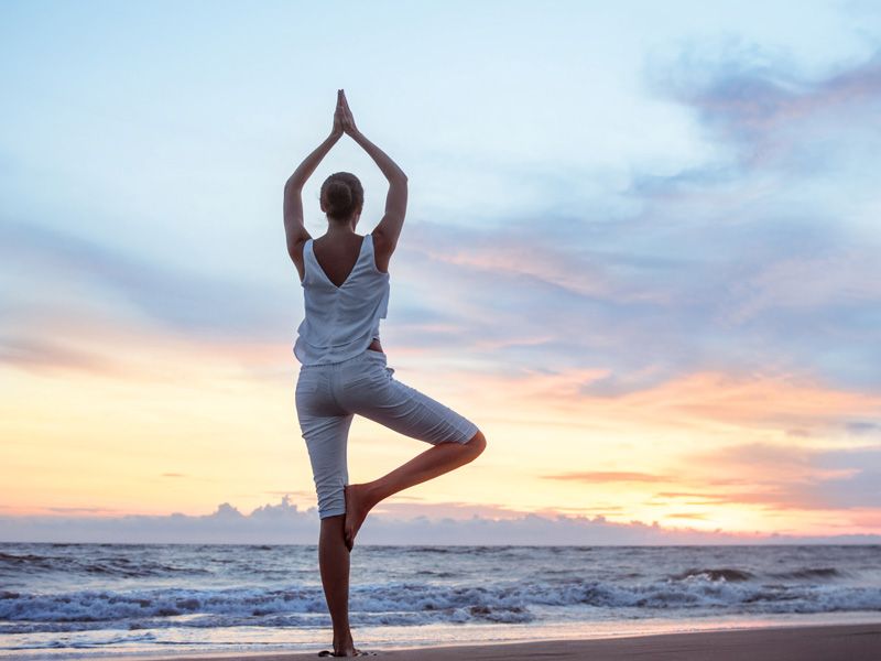 Imagem de uma mulher praticando yoga em frente a um belo pôr-do-sol em uma praia.