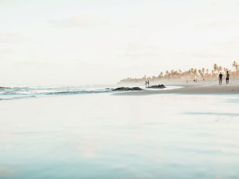 Imagem de uma praia com algumas pessoas andando na areia