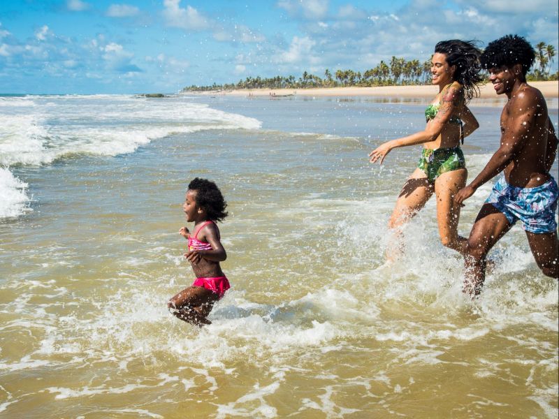 Imagem de dois adultos e uma criança se divertindo no mar