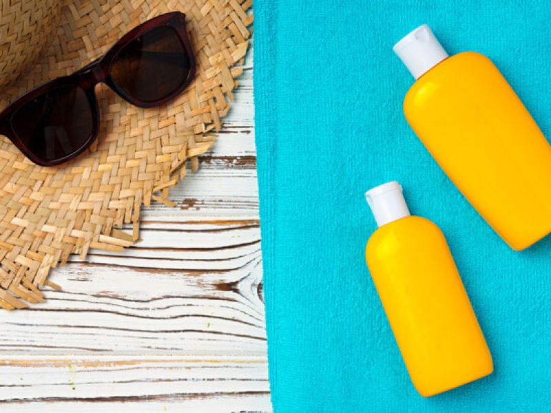 Imagem de alguns itens essenciais para ir a praia como protetor solar, óculos de sol, toalha e chapéu para se proteger do sol