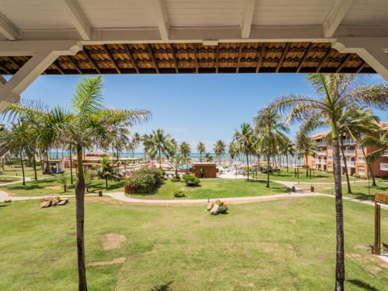 Imagem de resort all inclusive mostrando um grande gramado com coqueiros. No fundo, é possível ver a praia.