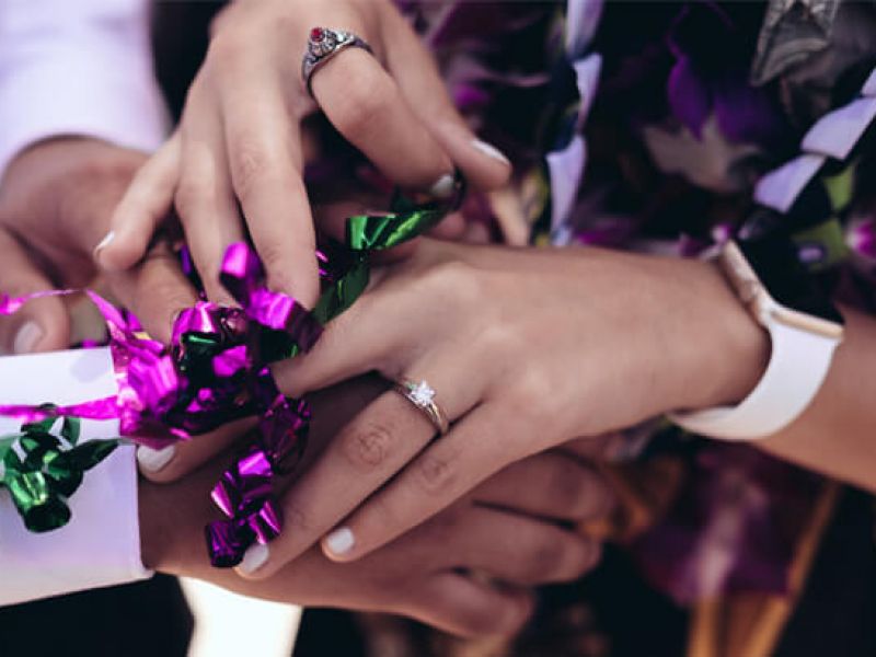 Imagem de dois pares de mãos. Uma das mãos está usando um anel de noivado e ambos os pares seguram confetes.