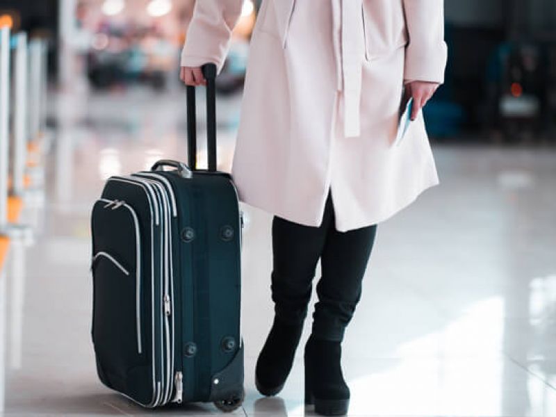 Imagem de uma pessoa segurando a alça de uma mala de rodinhas em um aeroporto.