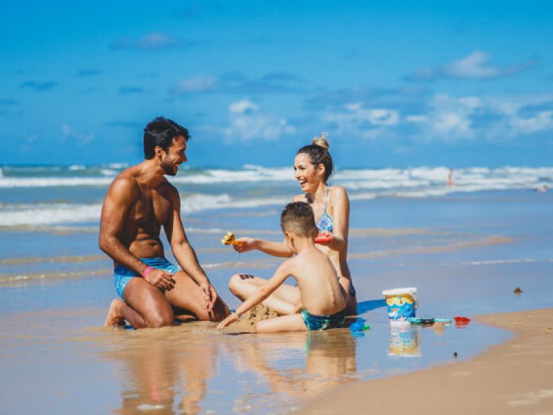 Imagem de uma mulher, um homem e uma criança se divertindo numa praia durante a viagem de férias em família.