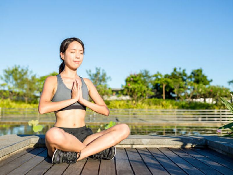 Imagem de uma mulher aprendendo como meditar ao lado de um lago.