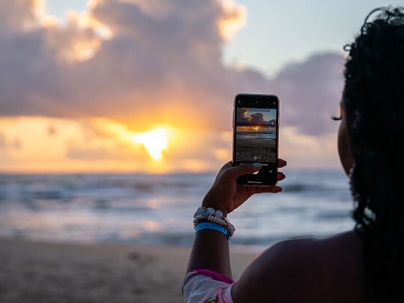 Imagem de uma pessoa tirando fotos de uma praia com o celular
