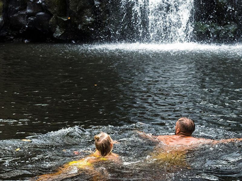 Imagem de duas pessoas nadando próximo a uma cachoeira