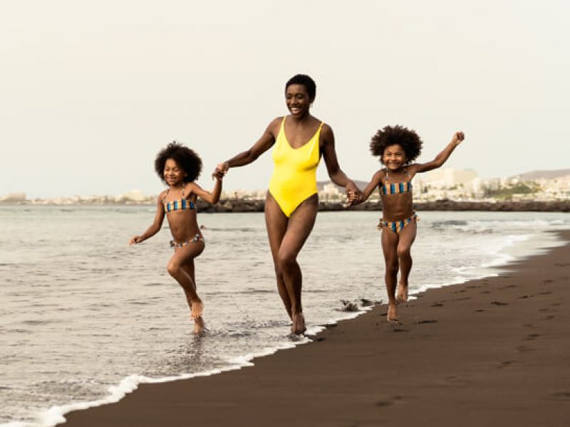 Imagem de uma mulher e duas crianças andando a beira-mar