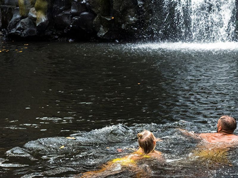 Imagem de duas pessoas nadando próximo a uma cachoeira