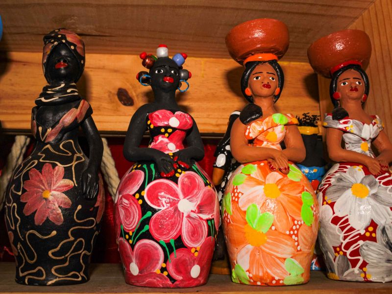 bonecas artesanais baianas em cerâmica, usando roupas coloridas e expostas em uma prateleira de madeira