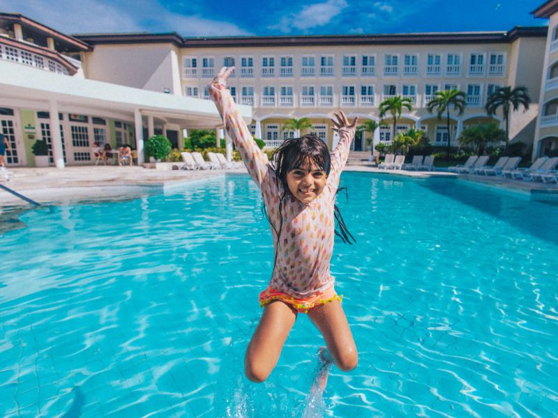 Criança saltando na piscina do Costa do Sauípe Resorts, com o hotel ao fundo