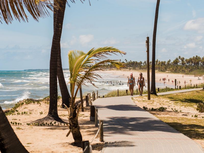 Duas mulheres caminhando pela estrada de madeira que leva da praia para o complexto de hotéis em Costa do Sauípe