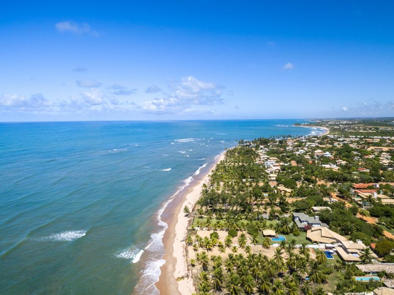 Orla da praia de Itacimirim, com as casas se misturando com a vegetação, enquanto o mar azul em contraste com a faixa de areia