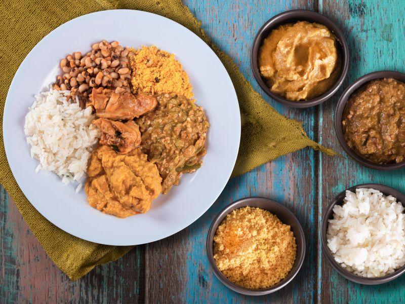 visão de cima de um prato sobre uma mesa de madeira. O prato tem comidas típicas do Brasil como arroz, feijão e caruru