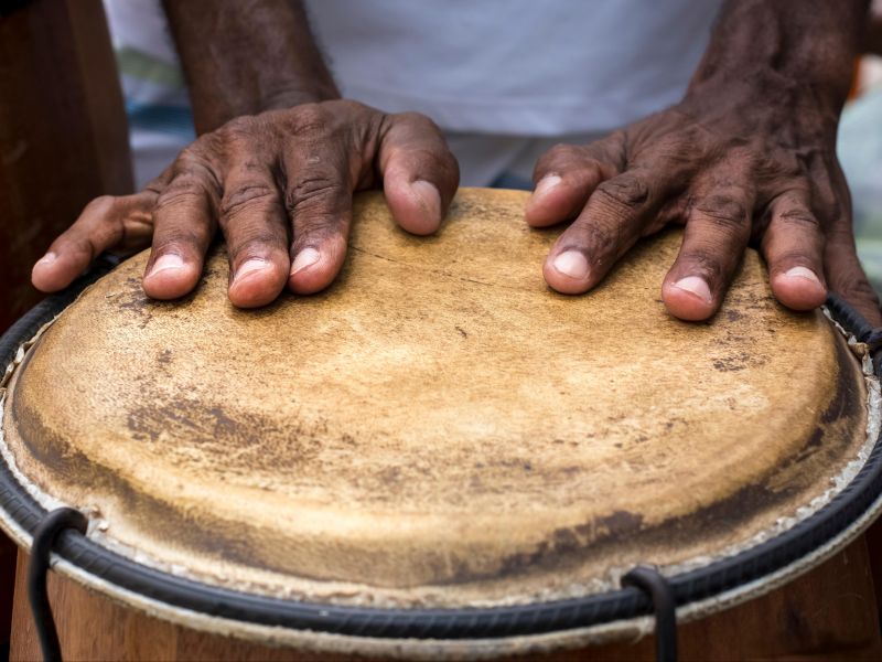 Parte das mãos de uma pessoa repousam sobre um tambor baiano