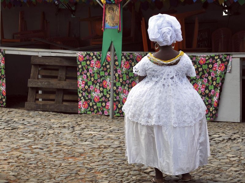 Baiana usando roupas tradicionais, de frente para um elemento de fé e oração