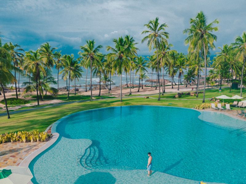 Pessoa parada em pé no meio de piscina no Costa do Sauípe, separada pelo mar apenas por coqueiros