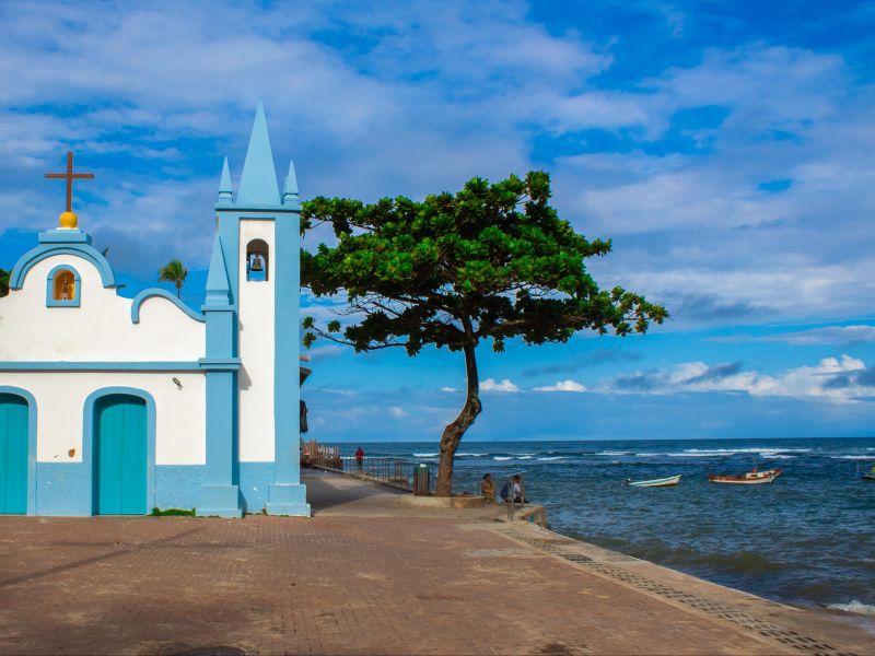 Igreja azul com o mar ao fundo, na Praia do Forte